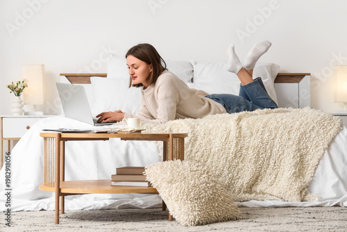 Beautiful young woman using laptop on bed in bedroom