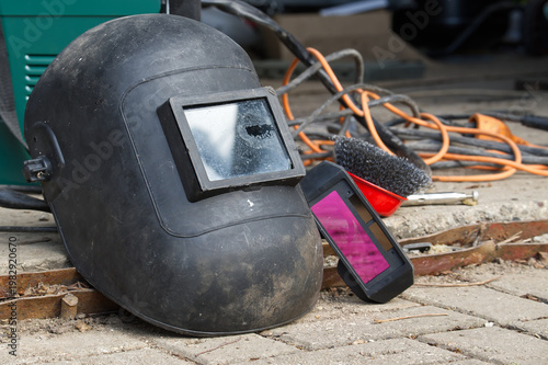 Welding helmet and equipment resting on a paved surface outdoors