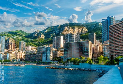 scenic cityscape of embarkment of Monte Carlo city in Monaco with blue sea water bay and amazing tall buildungs and houses along the coast. Urban mideterranean landscape with mountains and cloudy sky.