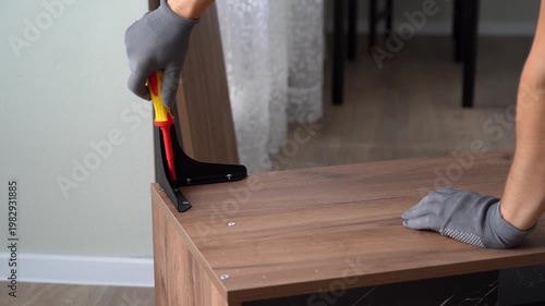 Hands assemble wooden nightstand using screwdriver. Installing metal furniture legs on coffee table. Process of assembling furniture