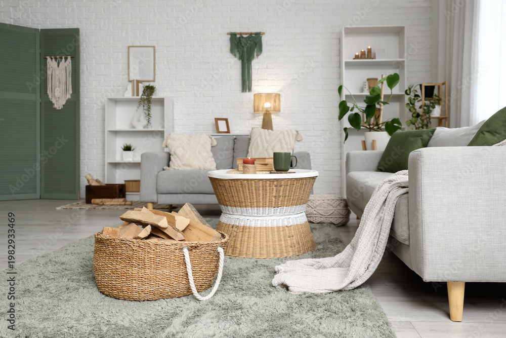 Naklejka premium Interior of living room with sofas, shelving units, coffee table and firewood in wicker basket