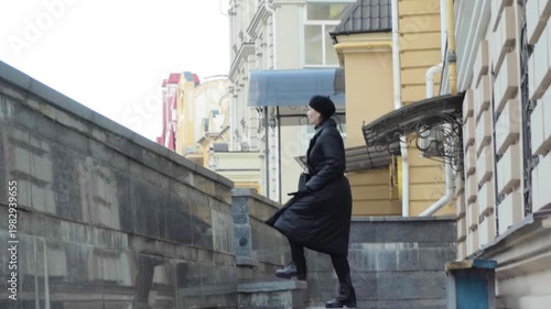 Elegant Woman in Black Coat Walking Up Stone Stairs in Urban European Cityscape