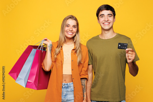 Young couple two friends family man woman wears casual clothes hold paper package bags after shopping credit bank card together isolated on plain yellow background. Black Friday sale buy day concept.