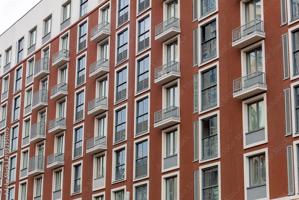 Obraz premium Modern apartment building with red brick and white accents. Windows face the sky with clean, uniform design. Balconies offer quiet views for residents. No people visible, so no emotions to describe