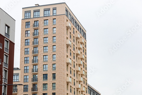 Modern apartment building stands tall against gray sky. Windows reflect city's quiet hum. Balconies offer views and everyday life. Clean lines suggest urban comfort
