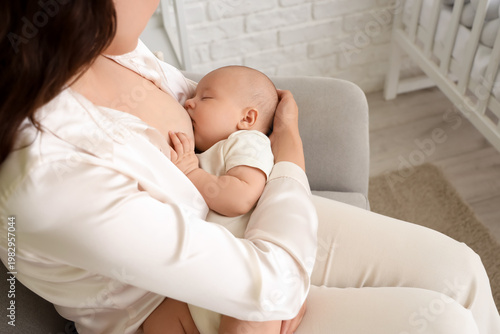 Young woman breastfeeding her little baby in armchair at home, closeup