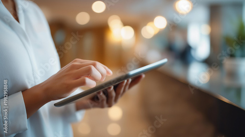 Faceless midsection of a hospitality manager using a bright tablet interface in a modern hotel lobby, defocused reception area, technology implementation, customer service innovation, digital