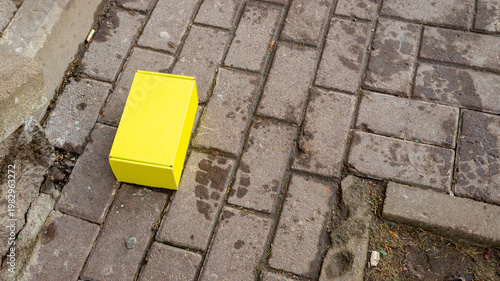Yellow cardboard box on wet gray paving stone. Parcel, delivery, Packaging concept or misplaced item. Urban street element.
