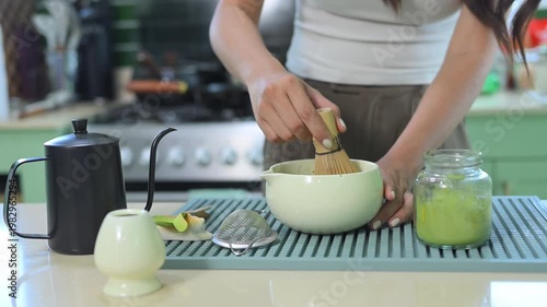 Close up of woman whisking matcha tea with bamboo chasen in kitchen.