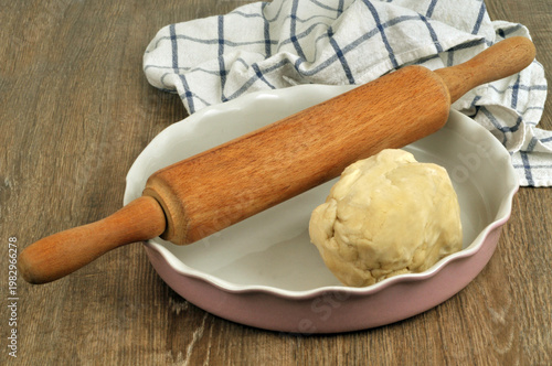 Pâte à tarte faite maison dans un plat avec un rouleau à pâtisserie et un torchon en gros plan sur un fond en bois