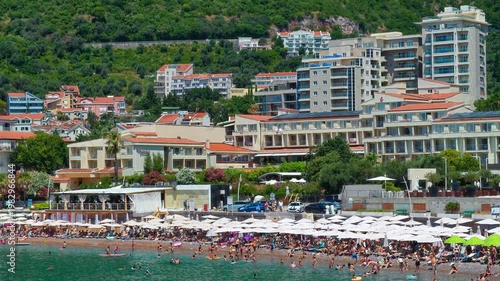 Sunny beach of Petrovac, Montenegro, featuring crystal clear turquoise water, white umbrellas, and Mediterranean architecture. A perfect summer vacation destination on the Adriatic coast
