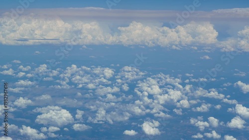 Stunning aerial view of fluffy white clouds against a bright blue sky during a daytime flight, capturing the beauty of air travel and the peaceful atmosphere of high altitude.
