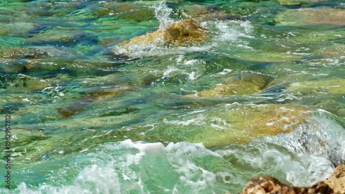 Crystal clear turquoise water washes over scenic layered rocks on the Mediterranean coast of Petrovac, Montenegro. A perfect summer travel background capturing the serene Adriatic Sea atmosphere.
