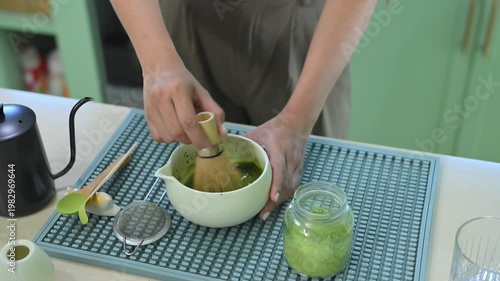 Close up of woman whisking matcha tea with bamboo chasen in kitchen.