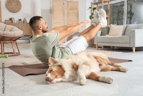 Bild auf Leinwand Sporty young man with Australian Shepherd dog training on mat at home