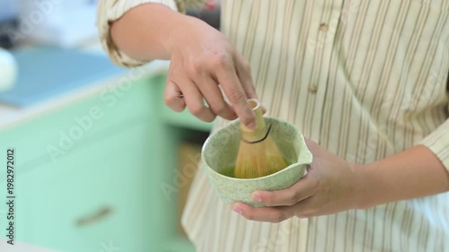 Close up of man whisking matcha tea with bamboo chasen in home kitchen.