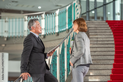 senior Confident business team discussing strategy on formal red carpet stair background. Senior executive leader with tablet and female colleague talking on red carpet steps for plan in luxury space