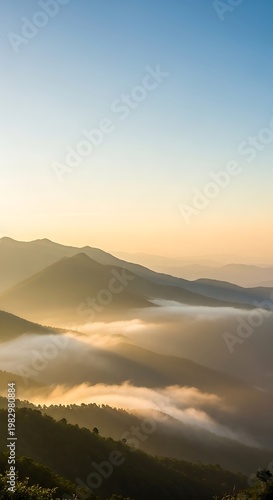 Misty mountain range at sunrise with golden light illuminating the peaks and valleys, creating a serene and breathtaking natural landscape.