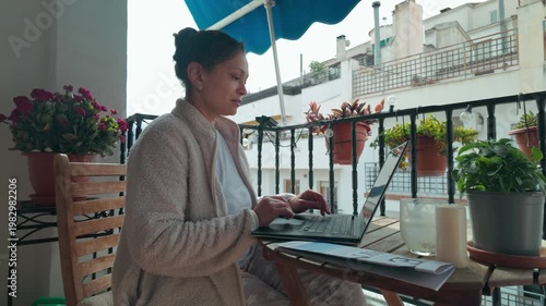 Woman Working Remotely on Laptop from a Sunny Balcony at Home
