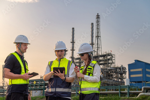 Obraz na płótnie Lead petroleum engineer in hardhat and vest holding tablet with radio pointing while briefing project to team at oil refinery site during sunset engineering teamwork planning in energy industry