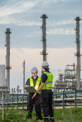 Two petroleum engineers discussing project and pointing direction with clipboard and radio communication at oil refinery site during sunset teamwork planning and industrial energy infrastructure.