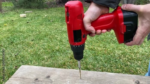 close up of cordless screwdriver removing screw from wooden surface reverse rotation diy repair and disassembly process power tool in action workshop detail