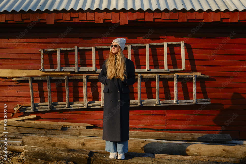 Obraz premium Young woman stands near wooden ladder in front of red barn during golden hour at rural location