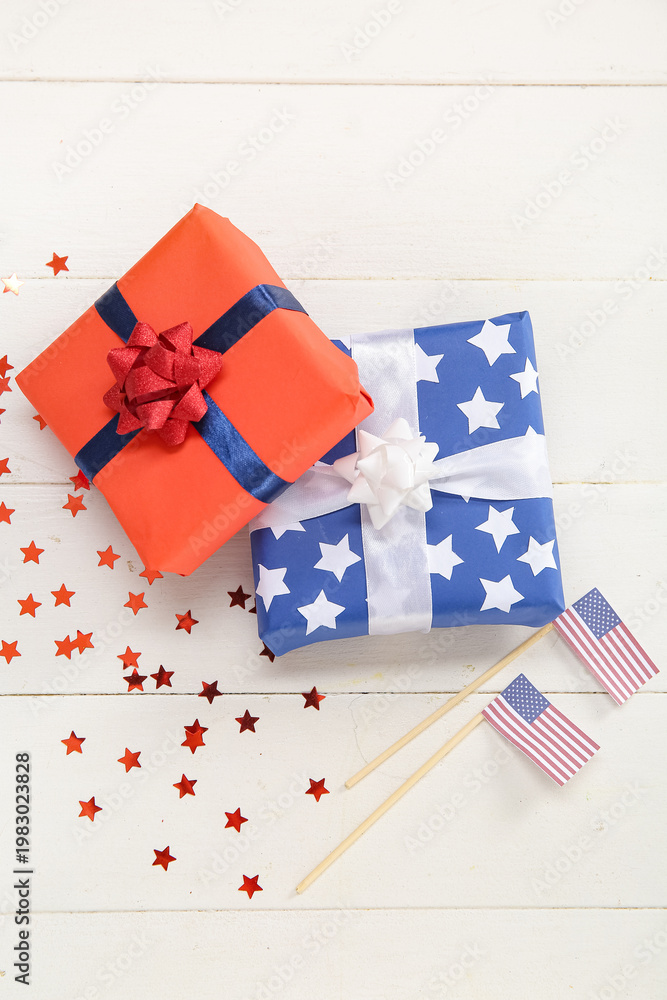 Obraz premium Gift boxes with USA flags and confetti on white wooden background. American Independence Day