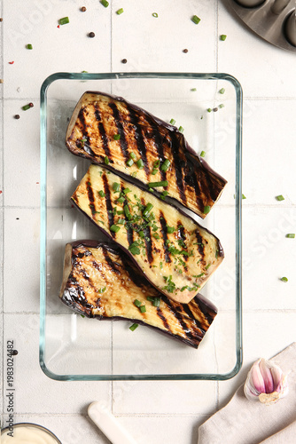 Glass casserole with delicious grilled eggplants on light background, top view