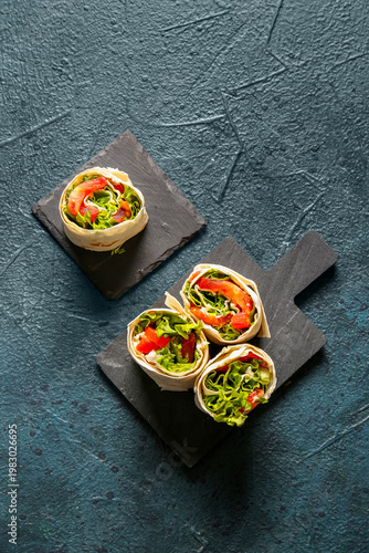 Boards of tasty lavash rolls with tomatoes and greens on black background