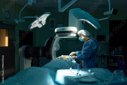Wide shot of surgeon performing minimally invasive procedure in operating room under imaging equipment, representing modern healthcare technology. Ideal for medical services marketing