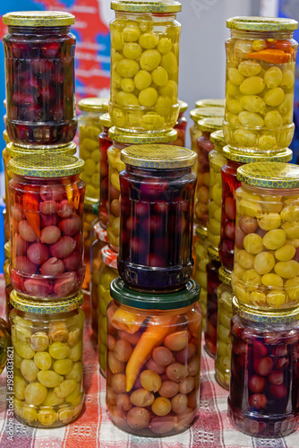 Selection of homemade pickled vegetables inside closed glass jars sold on market outdoors