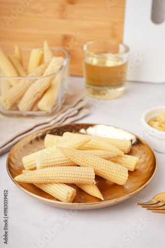 Plate with tasty canned corn cobs on light background