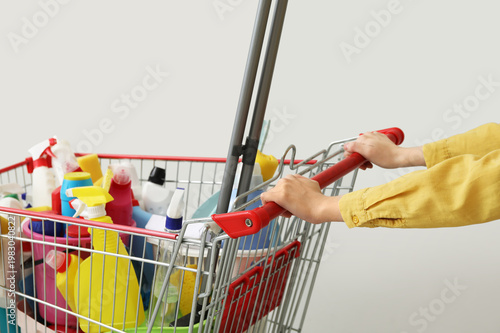 Photos Woman with cleaning supplies in shopping cart on light background