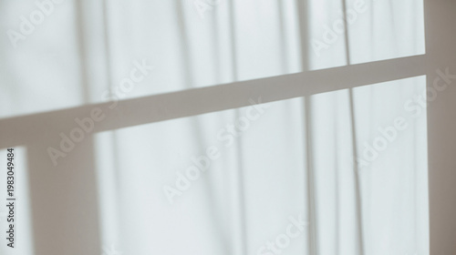 Shadows cast by window frames create geometric patterns across a plain interior wall surface during a bright and sunny afternoon.