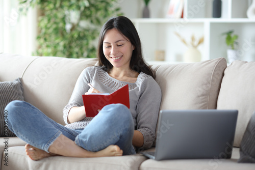 Free Download Happy asian woman writing in agenda beside laptop - GFXLoad