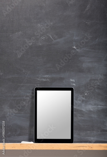 Digital tablet with blank screen standing on a wooden shelf against a dark chalkboard background.