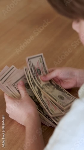 Hands counting and spreading fan of new US dollar bills on wooden desk, sorting banknotes, cash wealth and financial concept indoors close up overhead
