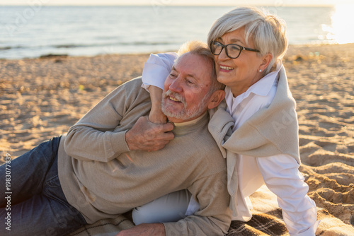 Bild auf Leinwand Senior mature couple sitting on beach hugging enjoying outdoor recreation