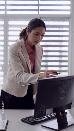 Asian adult female professional focused work computer desk modern office environment businesswoman reviewing document data analysis corporate setting productivity
