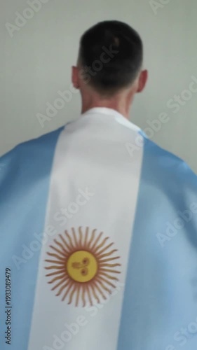 A man walks with an Argentine flag over his shoulders, seen from behind. A football fan supporting his national team