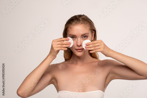 Fotografija Young woman completing daily skincare routine with cotton pads, cleansing and re
