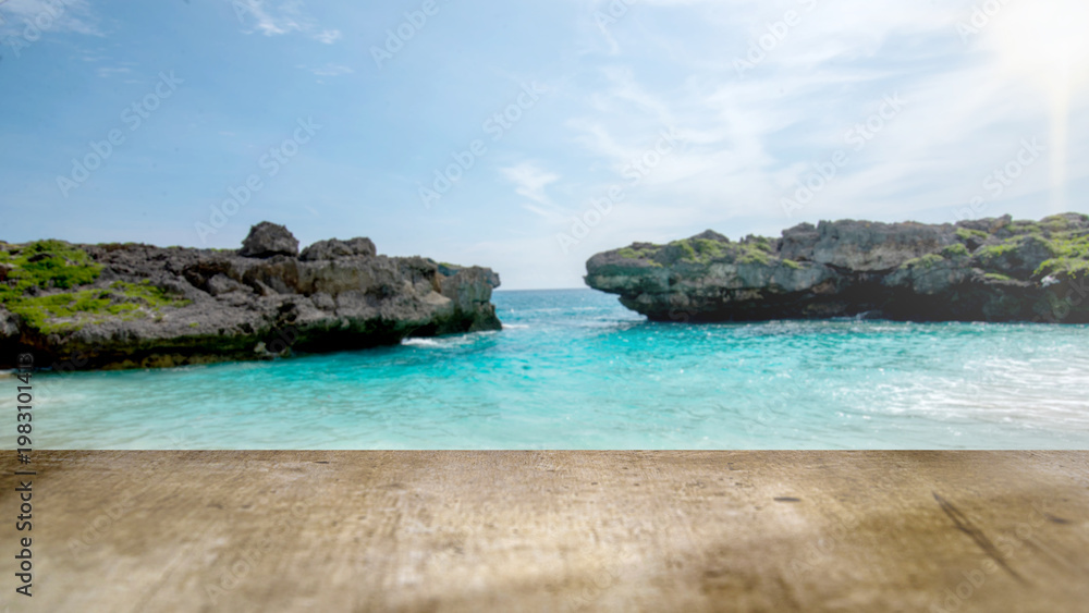 Naklejka premium Scenic tropical cove with clear turquoise water and rocky cliffs, seen from a rustic wooden table. Perfect for summer vacation, travel, and product placement backgrounds