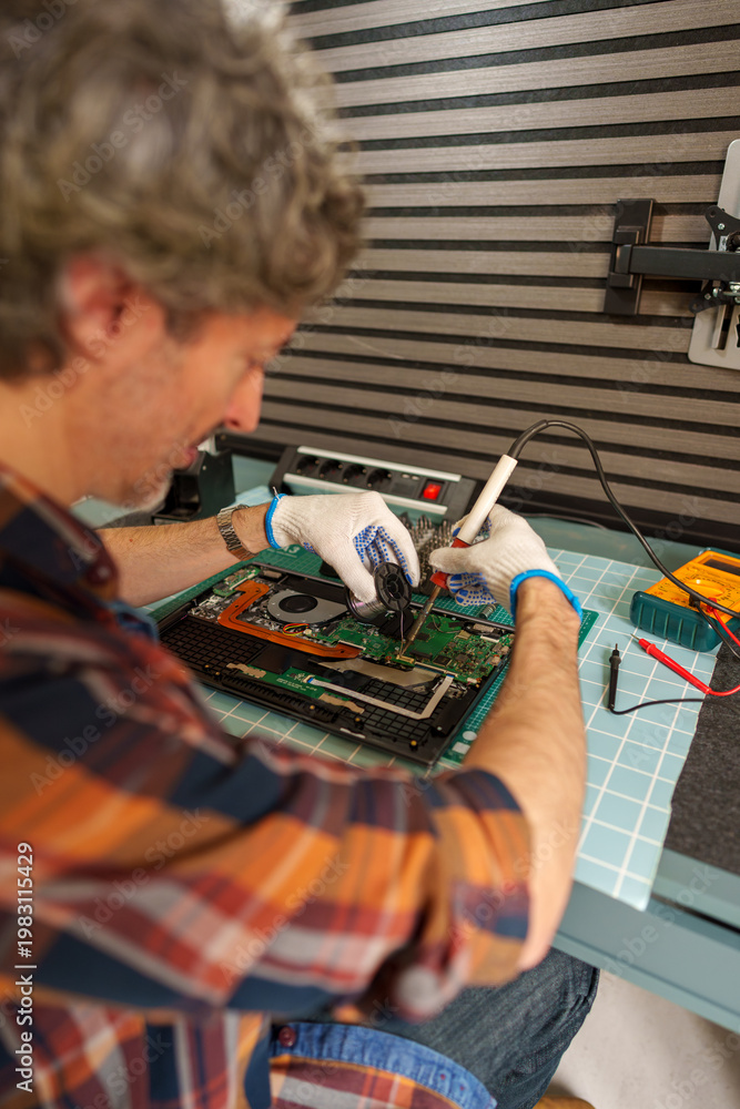 Fototapeta premium Man soldering electronic components on a laptop motherboard for repair and maintenance service