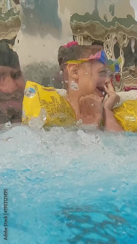 Happy family swim and laugh in blue summer pool under waterfall. Father and daughter fun play under stream of water. Travel vacation. Vertical shot