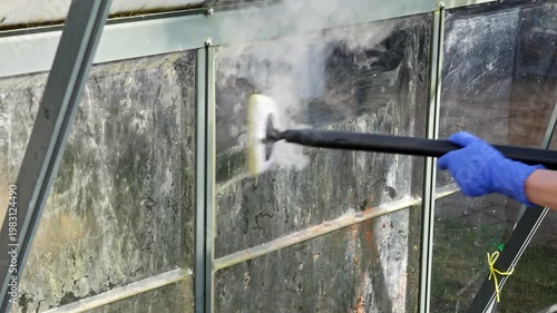 Close up view of woman cleaning greenhouse glass with steam cleaner during maintenance preparation for new season. Sweden.