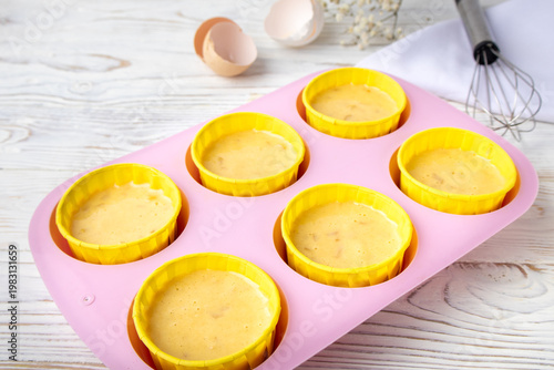 silicone mold with raw muffin batter on a white wooden table