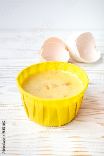 egg batter for a cupcake in a disposable paper mold on a white wooden table