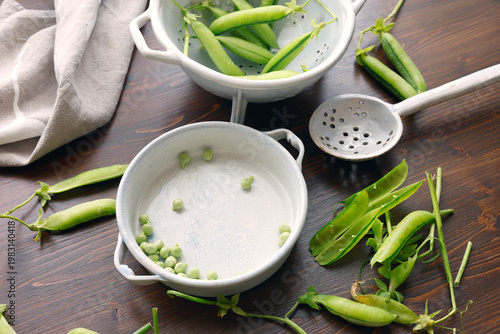 Fresh organic green peas being shelled in ceramic bowls on dark wooden table with copy space. High-angle shot features pea pods and individual peas highlighting seasonal harvest and healthy farm-to