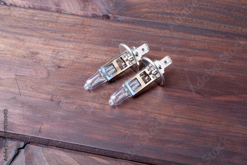 Two headlight bulbs are placed on a wooden surface. The bulbs are ready for use in a vehicle. The scene shows a simple preparation task at home.